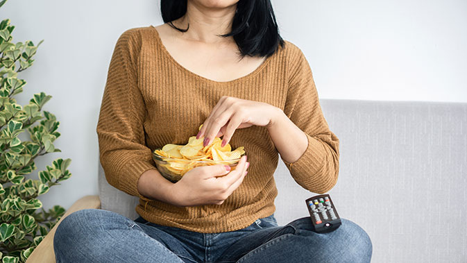 Eine Frau mit Heißhunger isst Chips auf dem Sofa.