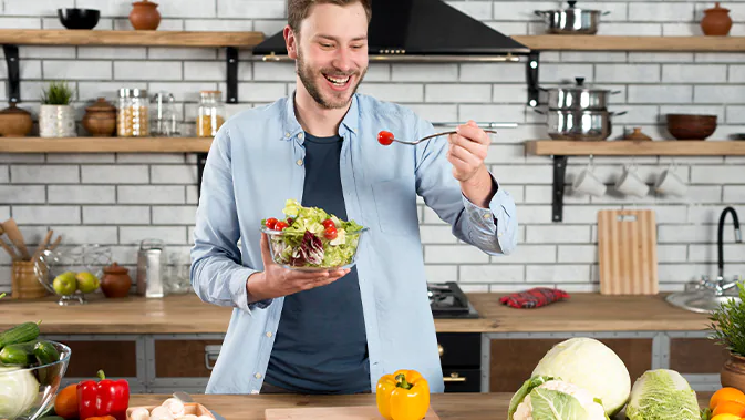 Ein Mann steht in einer Küche und isst einen bunten Salat