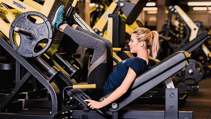 Sportliche Frau auf dem Gerät Beinpresse im Gym