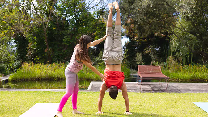 Frau hilft Mann dabei, einen Handstand zu halten.