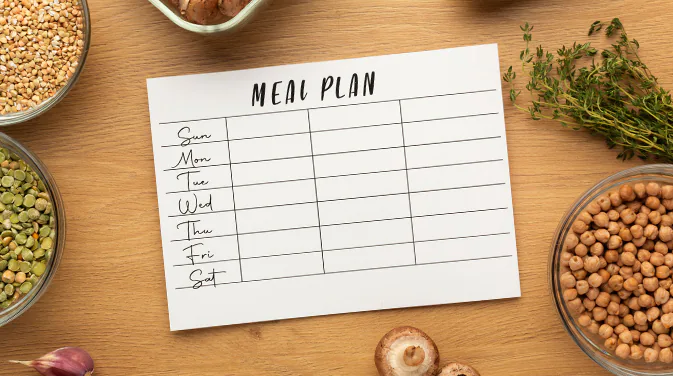 Ein Blatt Papier mit der Aufschrift Meal Plan liegt auf einem Tisch. Drumherum sind vegane Lebensmittel platziert: Linsen, Kichererbsen und Champignons