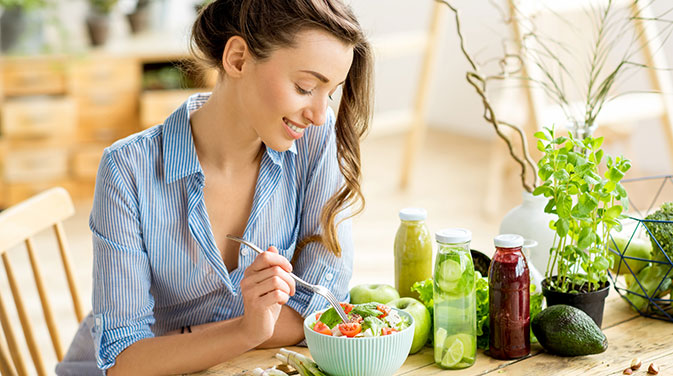Eine Frau isst einen bunten Salat. Daneben stehen verschiedene Säfte.