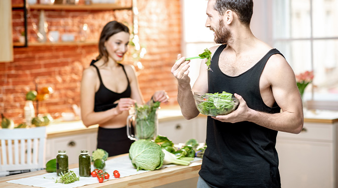 Mann und Frau in Sportkleidung in der Küche, der Mann isst Salat