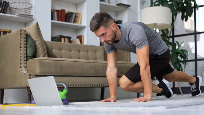 Mann trainiert im Wohnzimmer vor dem Laptop