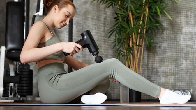 Frau in Sportkleidung massiert ihr Bein mit einer Massagepistole.