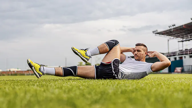 Das Krafttraining ist im Fußballsport nicht wegzudenken. Ein Fußballer macht SitUps auf dem Fußballplatz