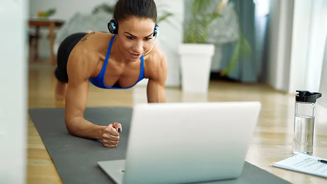 Frau vor dem Laptop auf einer Sportmatte in Plank-Position