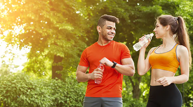 Mann und Frau in Sportkleidung im Wald, beide haben eine Flasche in der Hand.