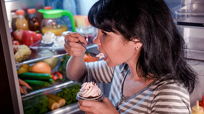 Frau steht am Kühlschrank und isst Dessert