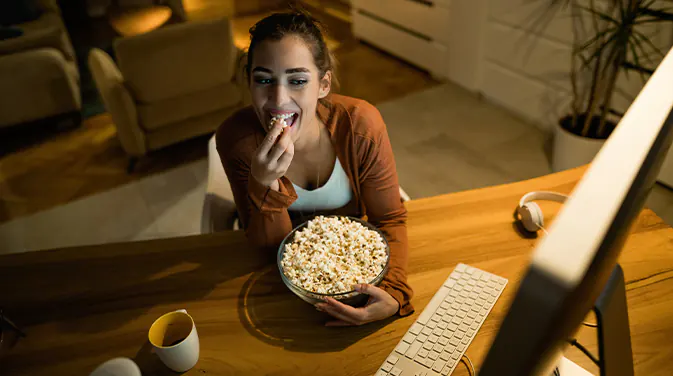 Frau isst Popcorn vor dem Computer