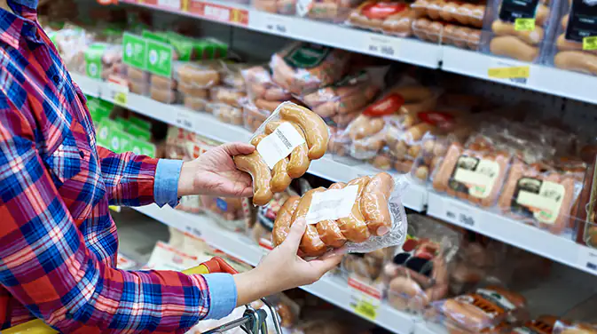 Frau im Supermarkt hält verpackte Würstchen in den Händen