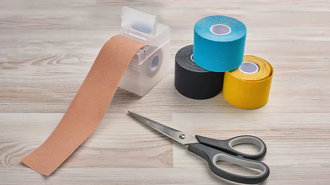 Verschiedene bunte und beigefarbene Kinesio-Tapes liegen auf einem Tisch, daneben eine Schere