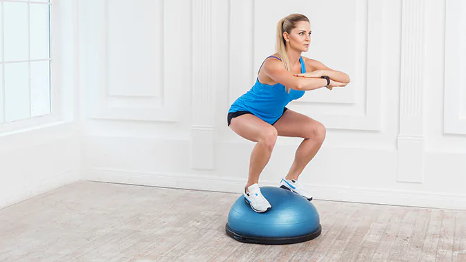 Eine Junge Frau in Sportkleidung macht eine Kniebeuge auf einem Balance Dome