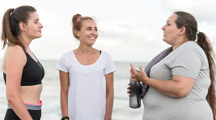 Drei Frauen mit unterschiedlichen Körpermaßen (schlank, durchschnittlich, übergewichtig) stehen zusammen und unterhalten sich.