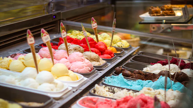 Eine Theke mit Speiseeis, in der viele verschiedene bunte Eissorten zu sehen sind.