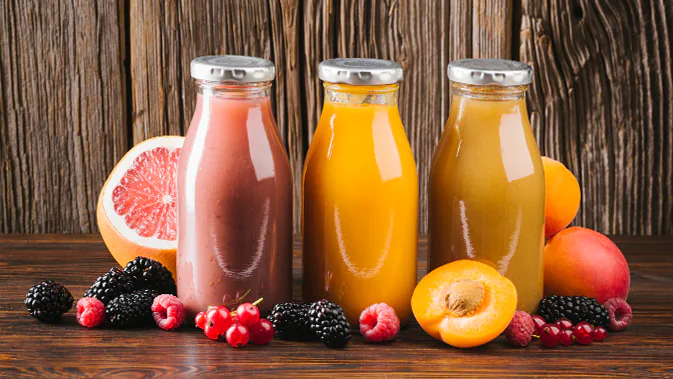 Drei verschiedenfarbige Säfte in Glasflaschen stehen nebeneinander. Um die Flaschen herum ist Obst abgebildet, z.B. Beeren, eine Grapefruit und Pfirsischhälften.