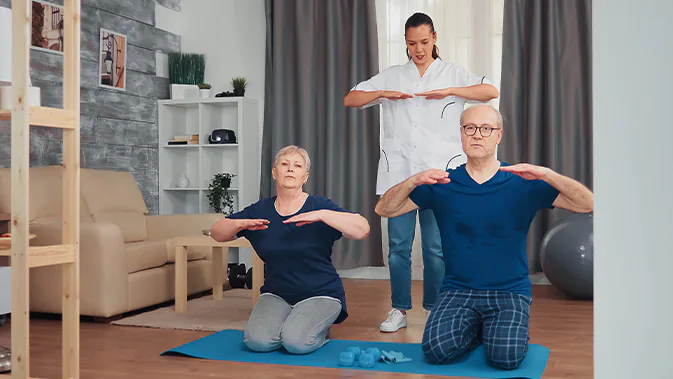 Eine Frau trainiert mit zwei älteren Menschen im Wohnzimmer.