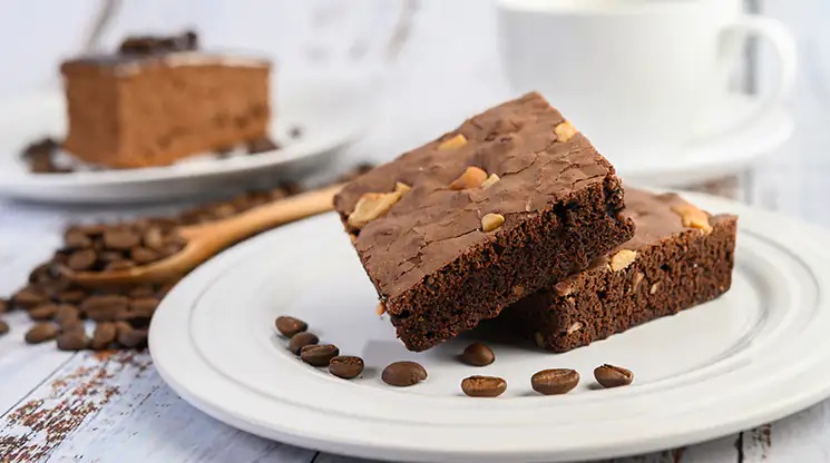 Mit glutenfreiem Mehl lassen sich zahlreiche glutenfreie Backwaren zubereiten. Zwei Brownies sind auf einem Teller übereinandergestapelt. Daneben liegen auf dem Teller ein paar Schokodrops.