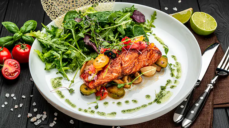 Fisch, Fleisch, Salat und Gemüse können bei einer Glutenunverträglichkeit problemlos verzehrt werden. Auf einem Teller ist ein Stück gebratener Fisch mit Gemüse und Salat angerichtet.