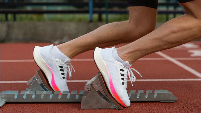 Man sieht die Schuhe und Beine eines Läufers in der Startposition auf einer Laufbahn