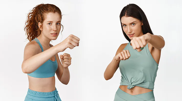 Zwei Frauen in sportlicher Kleidung stellen eine Pose wie beim Boxen nach.