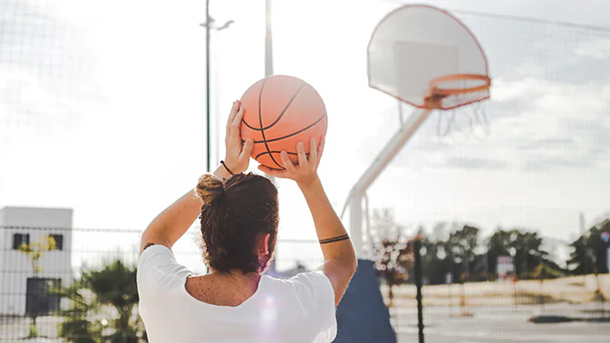 Eine männliche Person auf einem Outdoor-Basketballplatz setzt gerade zum Wurf an.