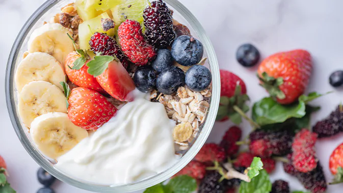 Eine Schüssel gefüllt mit Quark, Bananen, Erdbeeren, Heidelbeeren und Kiwi sowie Müsli.