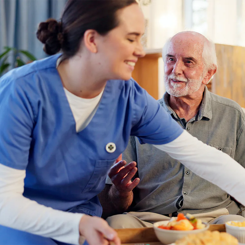 Pflegerin bringt einem Patienten eine vielfältige Mahlzeit - der Patient bedankt sich freundlich