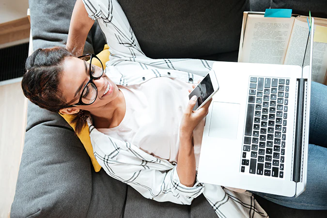 Frau liegt auf der Couch mit Laptop und Handy
