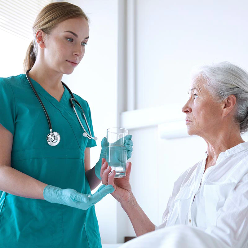 Eine Pflegerin reicht einer Patientin Tabletten und ein Glas Wasser