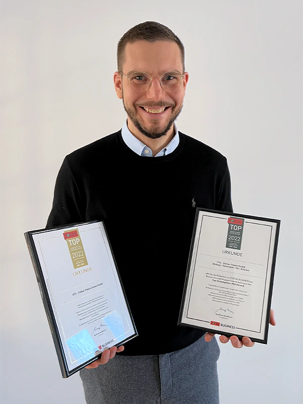 Geschäftsführer Daniel schaut in die Kamera und hält jeweils eine Urkunde von Focus Business in der Hand.