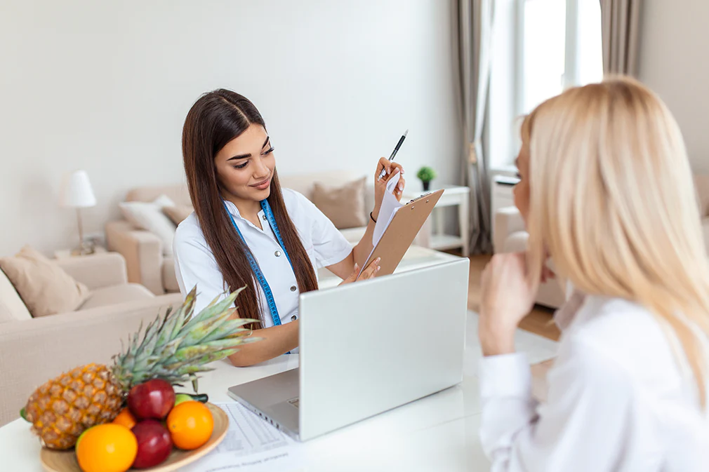 Ernährungsberaterin im Gespräch mit Patientin erklärt einen individuellen Ernährungsplan mit frischem Obst auf dem Tisch.