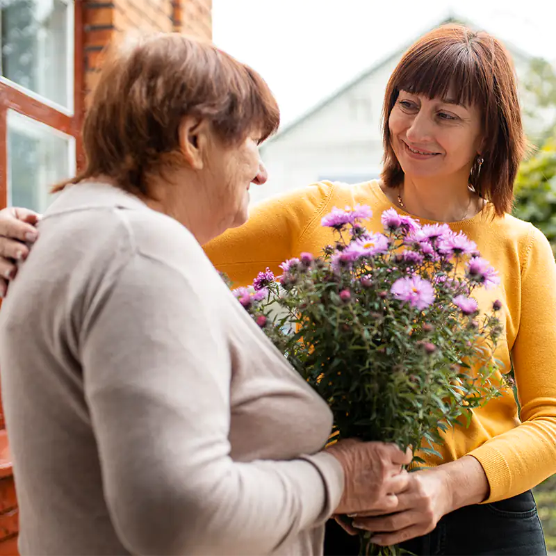 Trauerbegleiterin überreicht einer älteren Frau einen Strauß Blumen